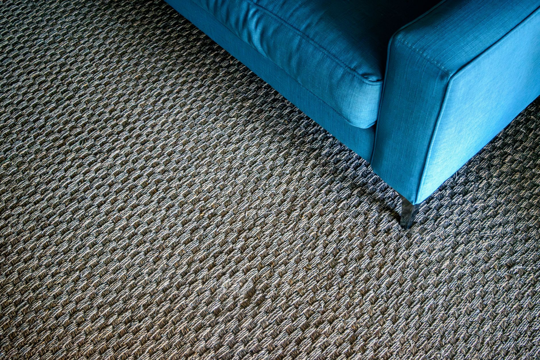 A modern blue sofa corner on a textured woven carpet, capturing a minimalist design